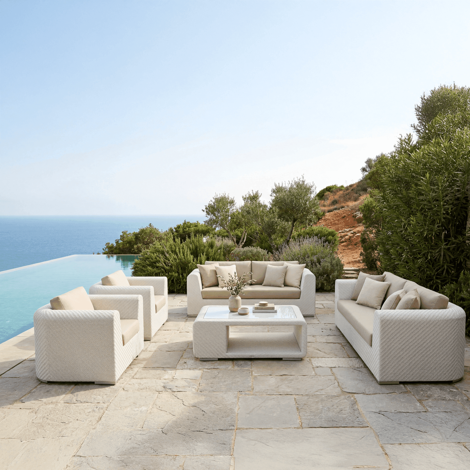 Woven outdoor lounge set with two sofas, two armchairs, and a coffee table on a stone terrace by an infinity pool and the.
