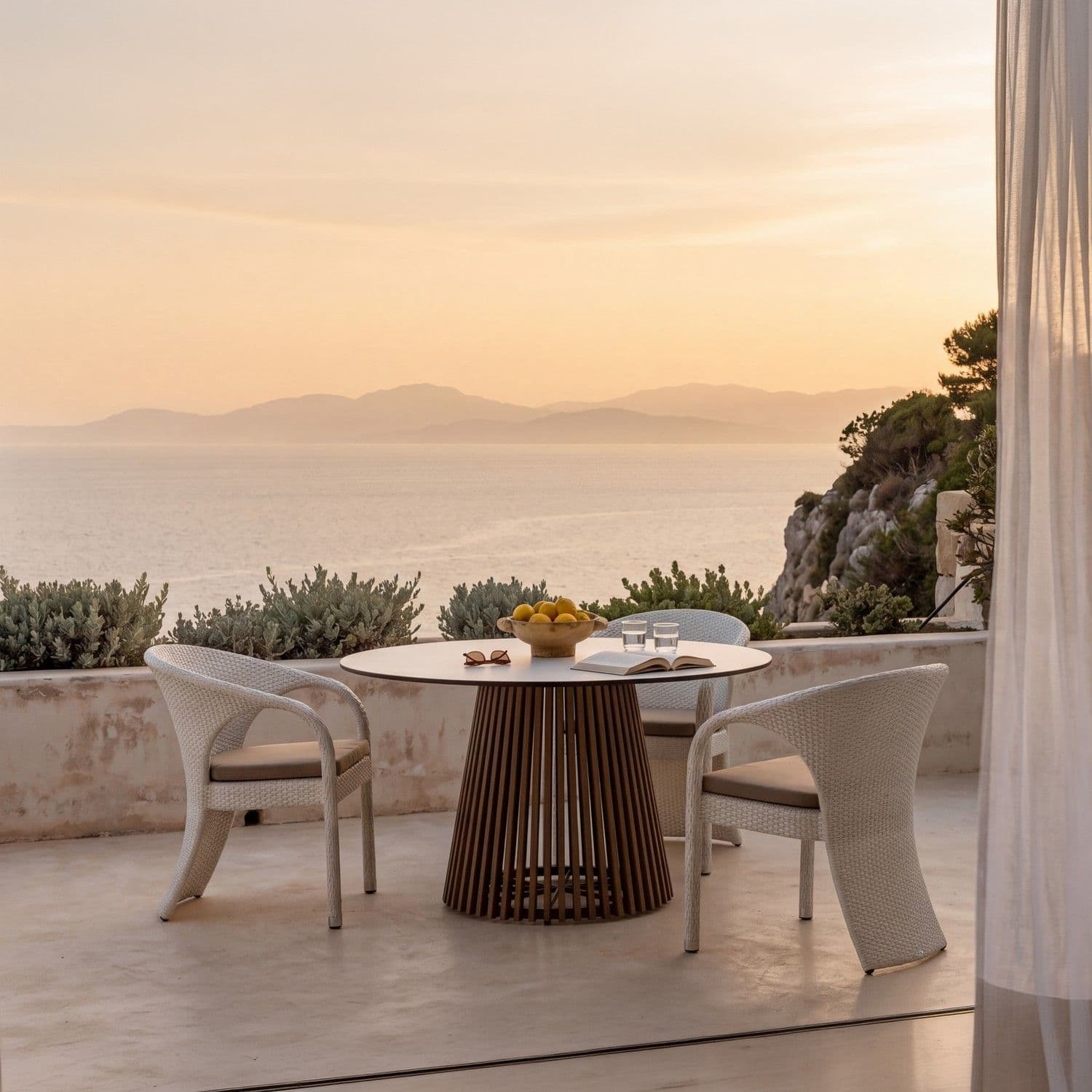 BLOOM Tuxedo juego de comedor de lujo: sillas tejidas artesanales y mesa premium en una terraza costera con vistas al mar.