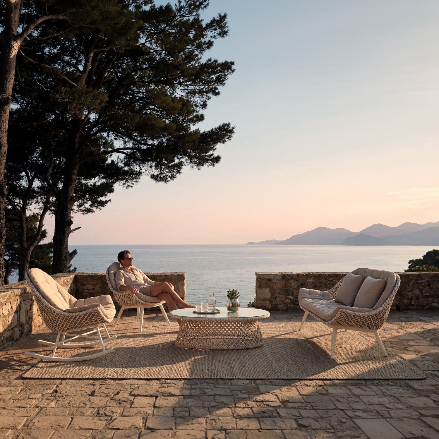 BLOOM Muse muebles de exterior de lujo: mecedora, sillón, mesa de centro. Mobiliario premium en terraza con vistas al mar.